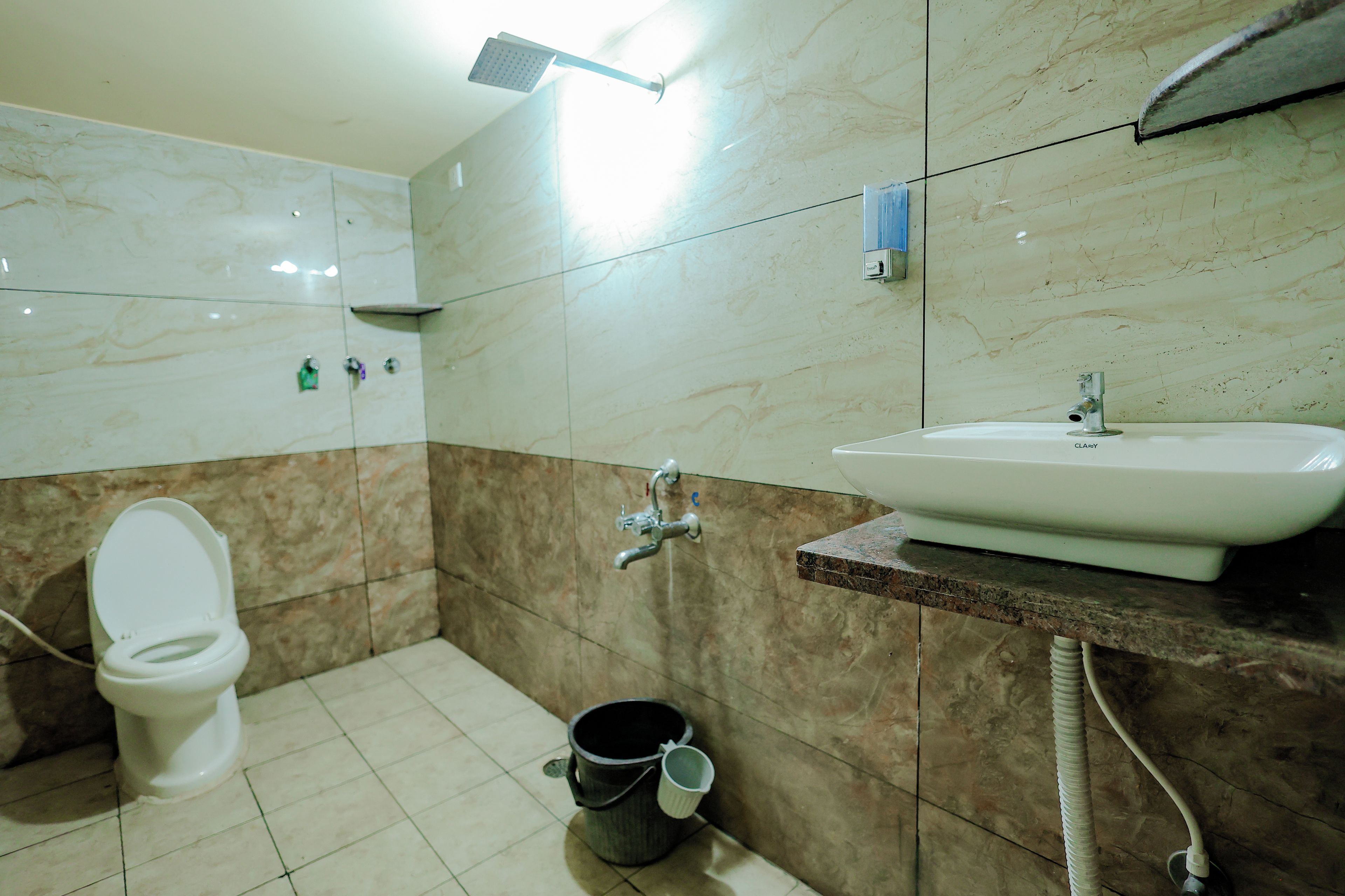 A bathroom with a toilet, sink, shower, and a bucket.