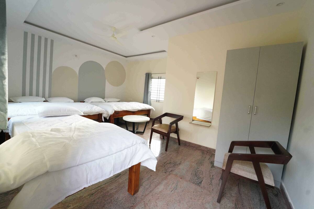 A hotel room with three beds, a small round table, a chair, and a wardrobe.