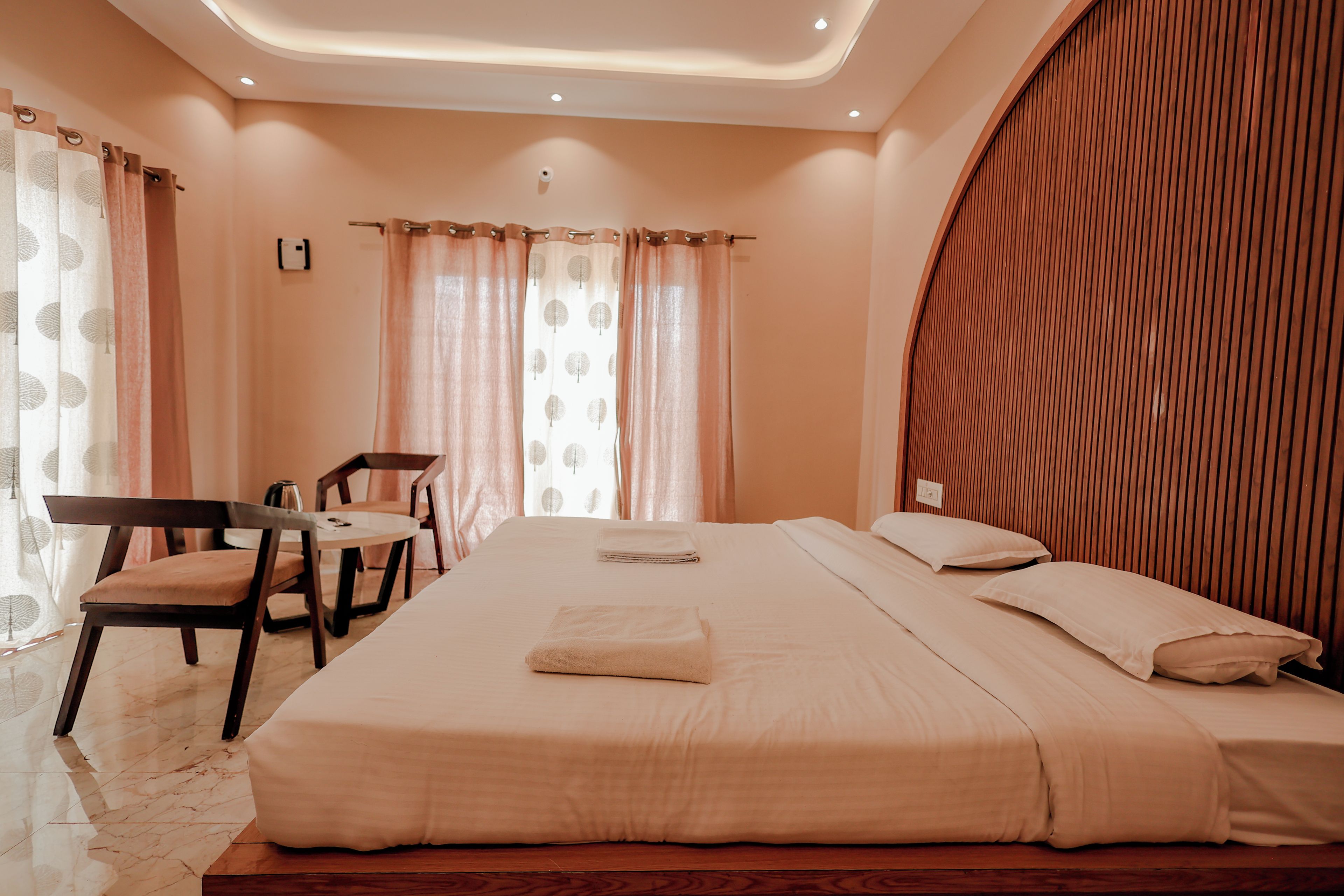 A hotel room with a large bed, a wooden headboard, a desk with a chair, and a window with curtains.