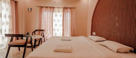 A hotel room with a large bed, a wooden headboard, a desk with a chair, and a window with curtains.