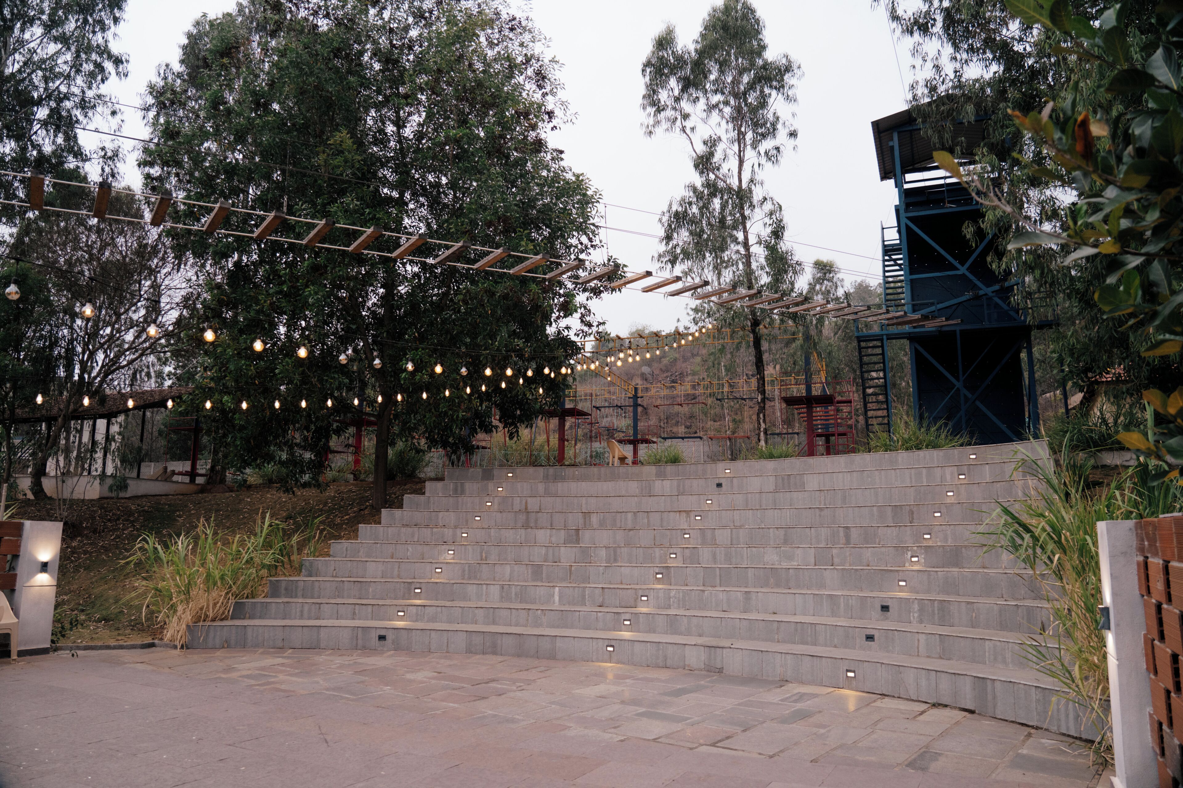 A set of outdoor stairs with string lights, surrounded by trees and a brick wall.