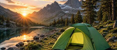 A green tent by a lake with mountains in the background.