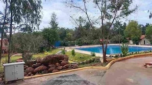 A swimming pool surrounded by trees and a small building. - Benchkal Resort (Tumkur)