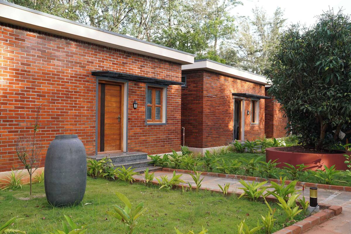 A modern brick house with a well-maintained garden, a large grey planter, and a small tree.