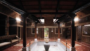 A room with a central square area, wooden pillars, a large vase, and hanging light fixtures. - Benchkal Resort (Tumkur)