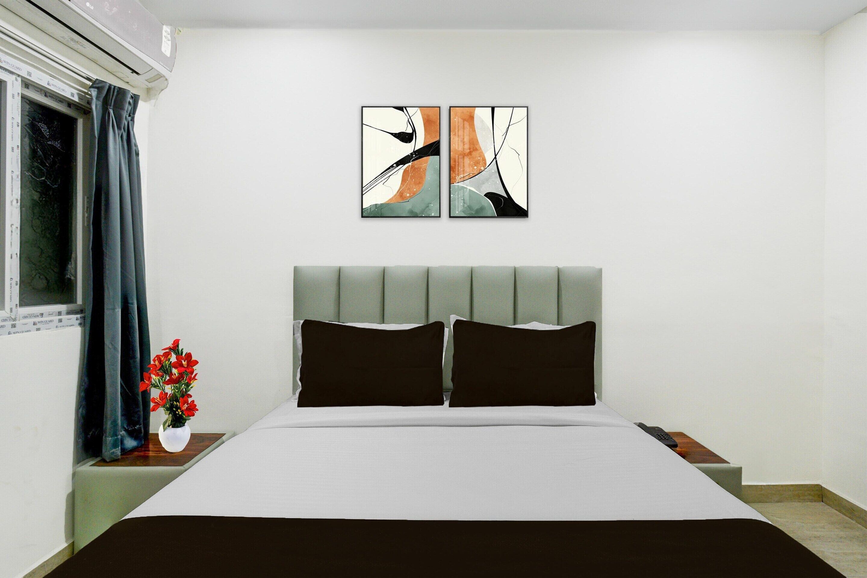 A bedroom with a bed, a nightstand, a vase with flowers, abstract wall art, and a window with curtains.