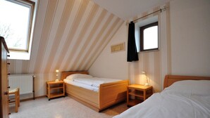 Een slaapkamer met een schuine kap, twee bedden, een radiator en een raam.