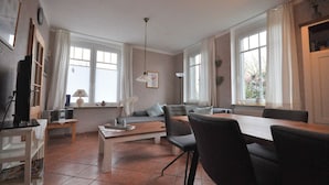 A modern living room with a dining area, large windows, and a ceiling fan. - Land-Domizil terraced house 1 - Terraced house Land-Domizil 1 (Werdum)