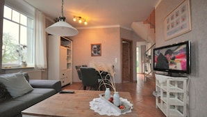 A living room with a sofa, coffee table, TV, and a dining area with chairs and a table. - Land-Domizil terraced house 1 - Terraced house Land-Domizil 1 (Werdum)