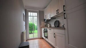 A kitchen with white cabinets, a tiled backsplash, and a view through a sliding glass door to a garden. - Land-Domizil terraced house 1 - Terraced house Land-Domizil 1 (Werdum)