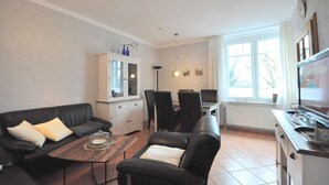 Ett vardagsrum med en soffa, stolar, ett skåp, ett matbord och en tv.