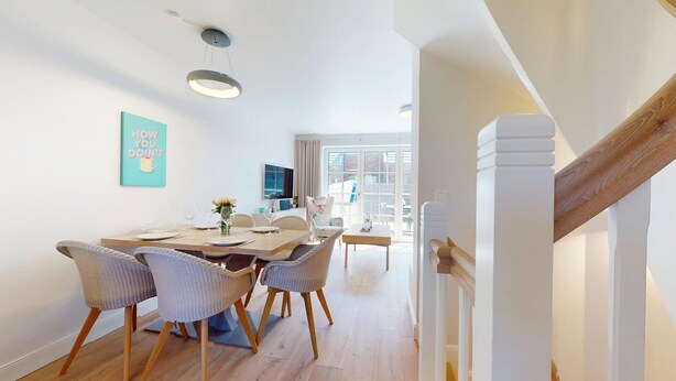 Een eetruimte met een houten tafel, rieten stoelen en een schilderij aan de muur.