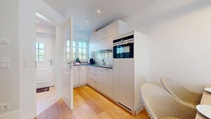 Een moderne keuken met witte kasten, een inbouwoven en een eethoek met rieten stoelen.