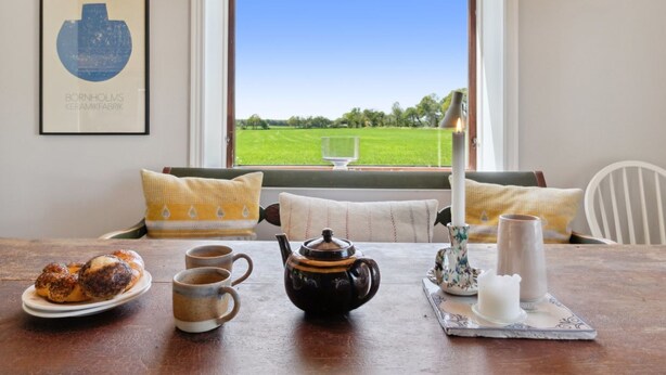 A cozy dining area with a table set for breakfast, a window with a view of a green field, and a framed artwork on the wall. - "Aarni" - 6.5km from the sea by Interhome (Gudhjem)