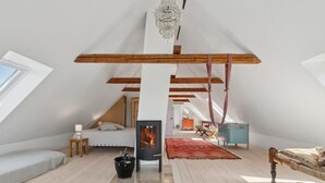 A spacious attic bedroom with a sloped ceiling, exposed wooden beams, a large window, a bed, a fireplace, and a hanging chair. - "Aarni" - 6.5km from the sea by Interhome (Gudhjem)