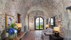 A stone-walled room with a sofa, two lamps, a table with a vase of flowers, and a view through a large arched window. - Villa in Badia A Passignano with 9 bedrooms sleeps 18 (Badia A Passignano)
