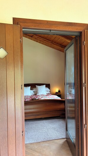 A bedroom with a wooden bed, a nightstand, and a sliding glass door leading to another room. - Panoramic two-story dwelling with private garden, surrounded by green woods. (Piemonte)