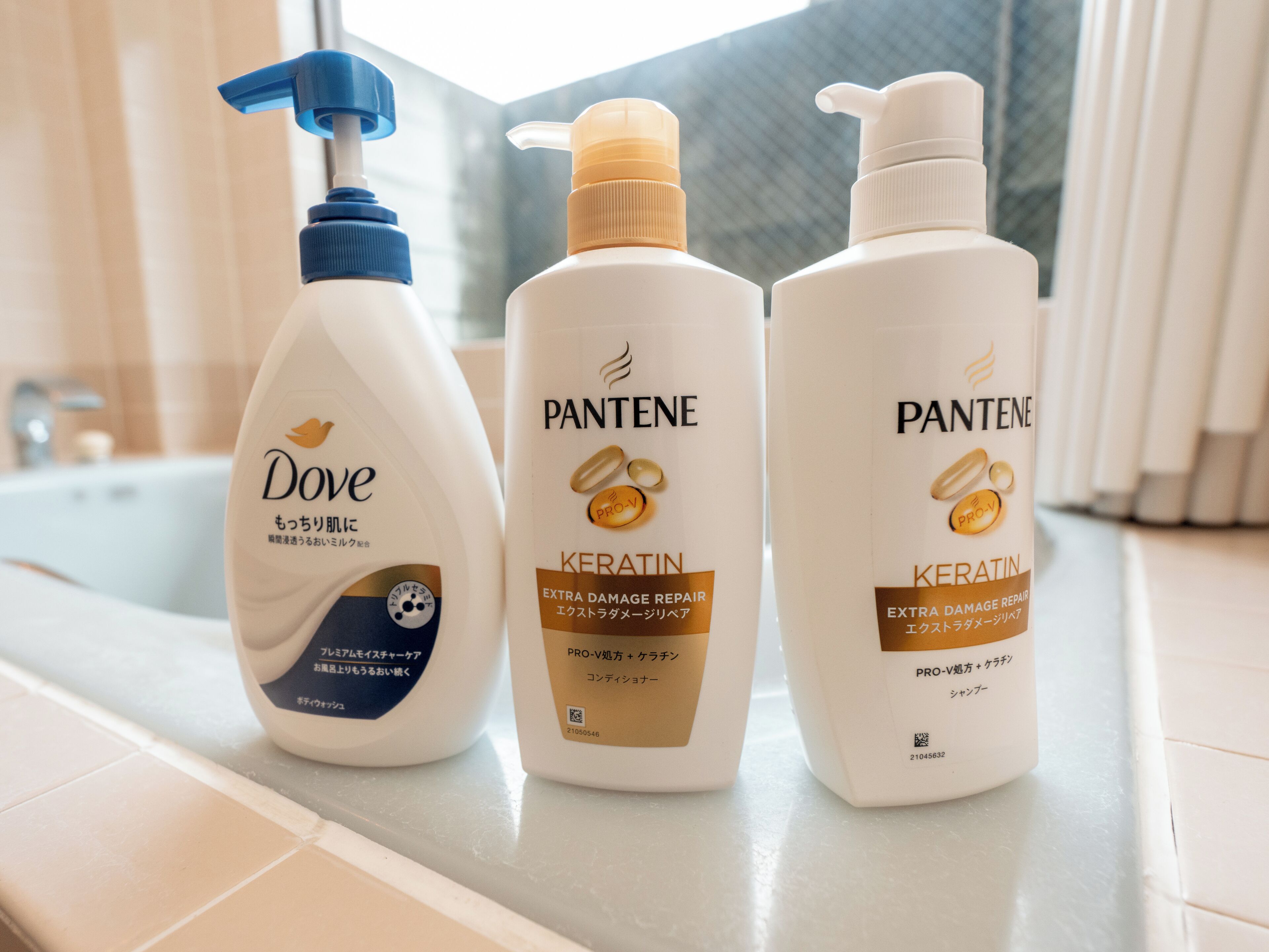 Three bottles of Dove and Pantene hair care products on a bathroom counter.