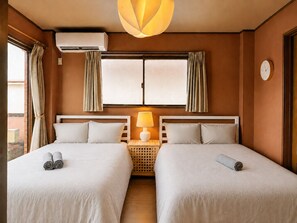 Habitación de hotel con dos camas, una ventana con cortinas, un equipo de aire acondicionado, una lámpara y un reloj en la pared.