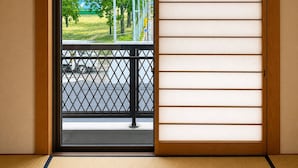Una habitación con puerta corredera tipo shoji, suelo de tatami y vista a una calle con árboles y un semáforo.