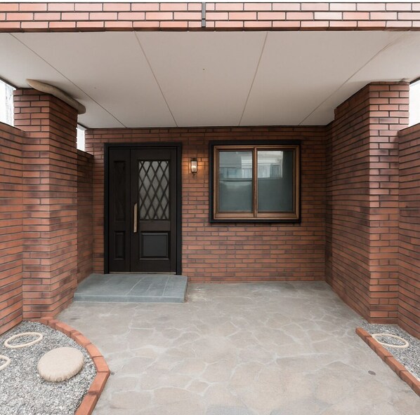 Fachada de ladrillo con una puerta negra, una ventana y un pequeño porche con escalones.