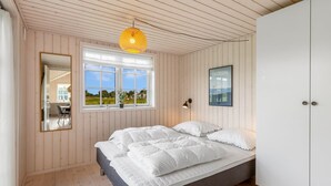 A bedroom with a bed, a window, a mirror, a hanging light fixture, and a wardrobe.