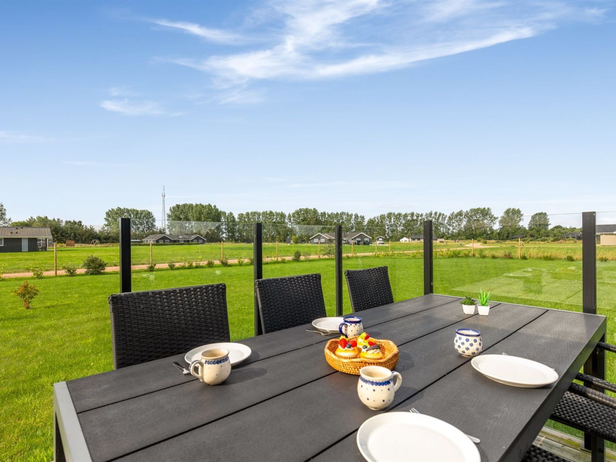 A table set outdoors with chairs, a basket of food, and tableware.