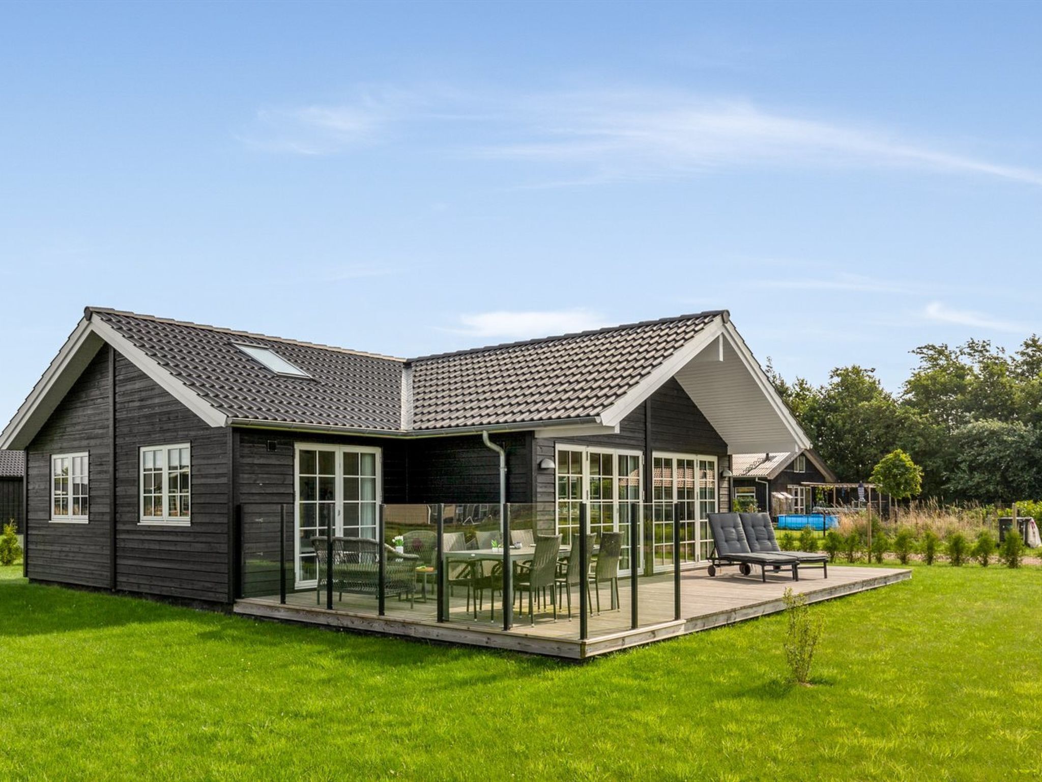 A modern house with a covered patio, a swimming pool, and a well-maintained lawn.