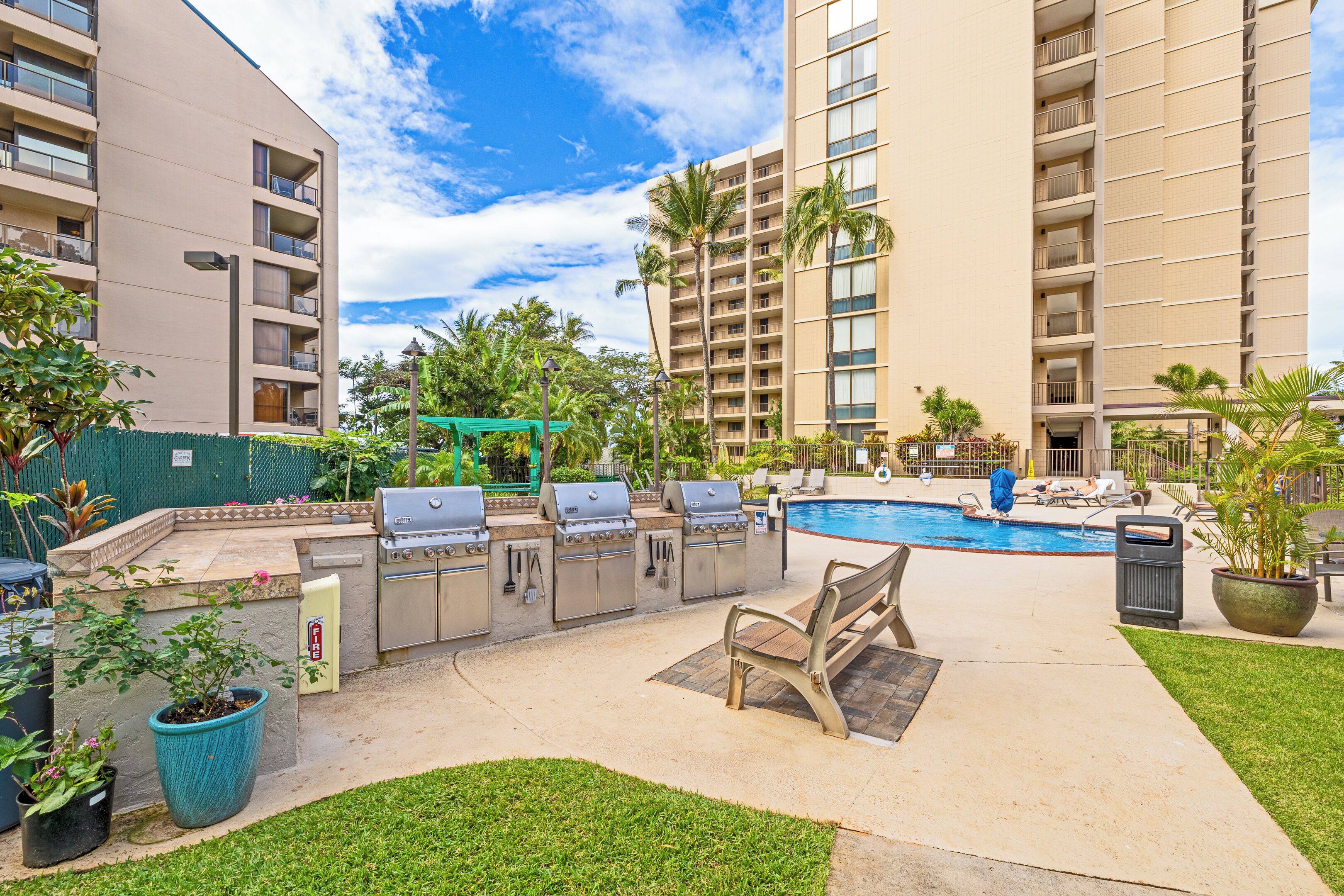 An outdoor pool area with a barbecue setup, lounge chairs, and a grassy lawn.