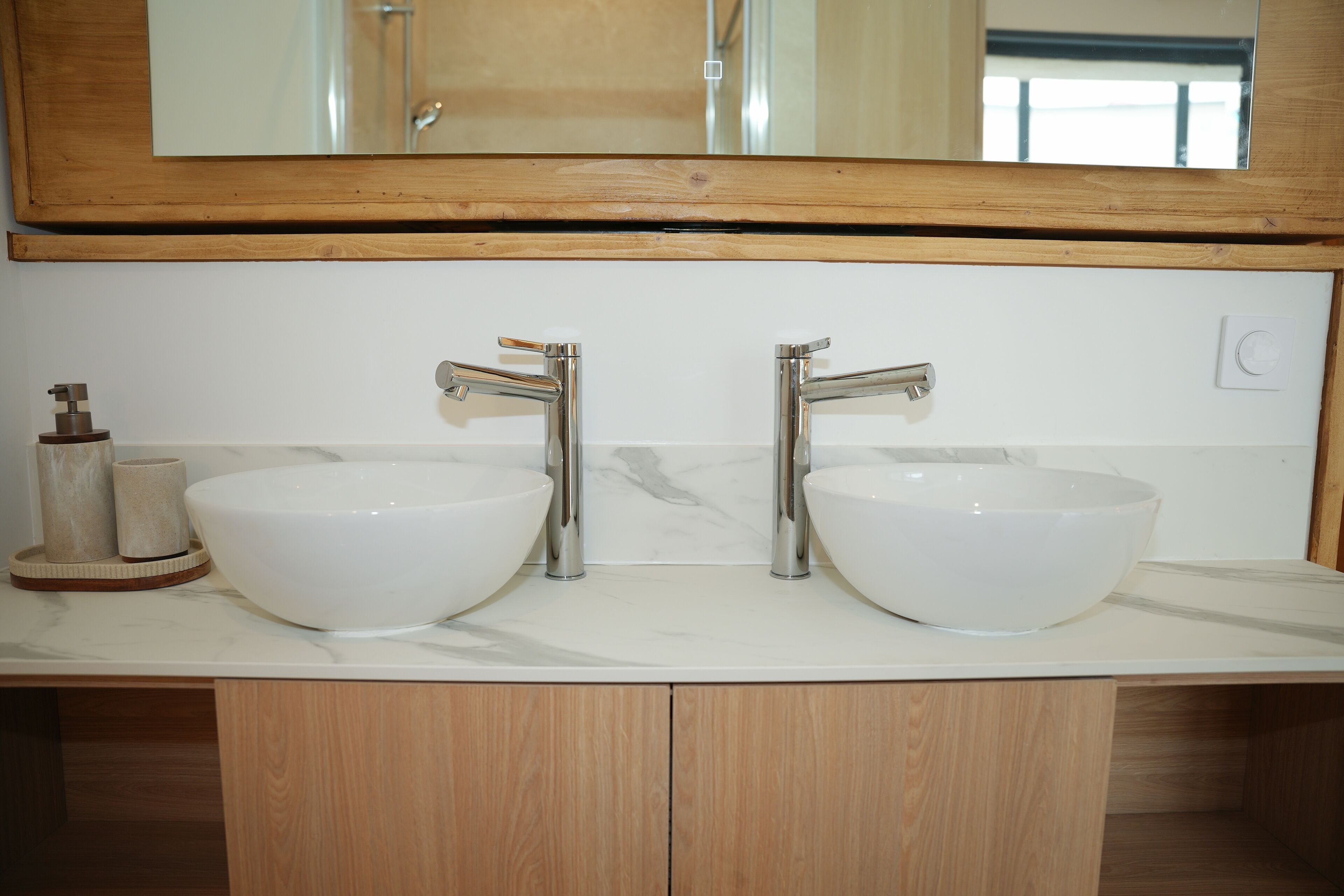 A bathroom with two white ceramic sinks, wooden cabinets, and a large mirror above the sinks.