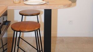 A modern kitchen with a wooden table, two stools, and a glass.