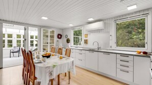Une cuisine moderne avec des meubles blancs, une table à manger avec des chaises et une grande fenêtre donnant sur un paysage verdoyant.