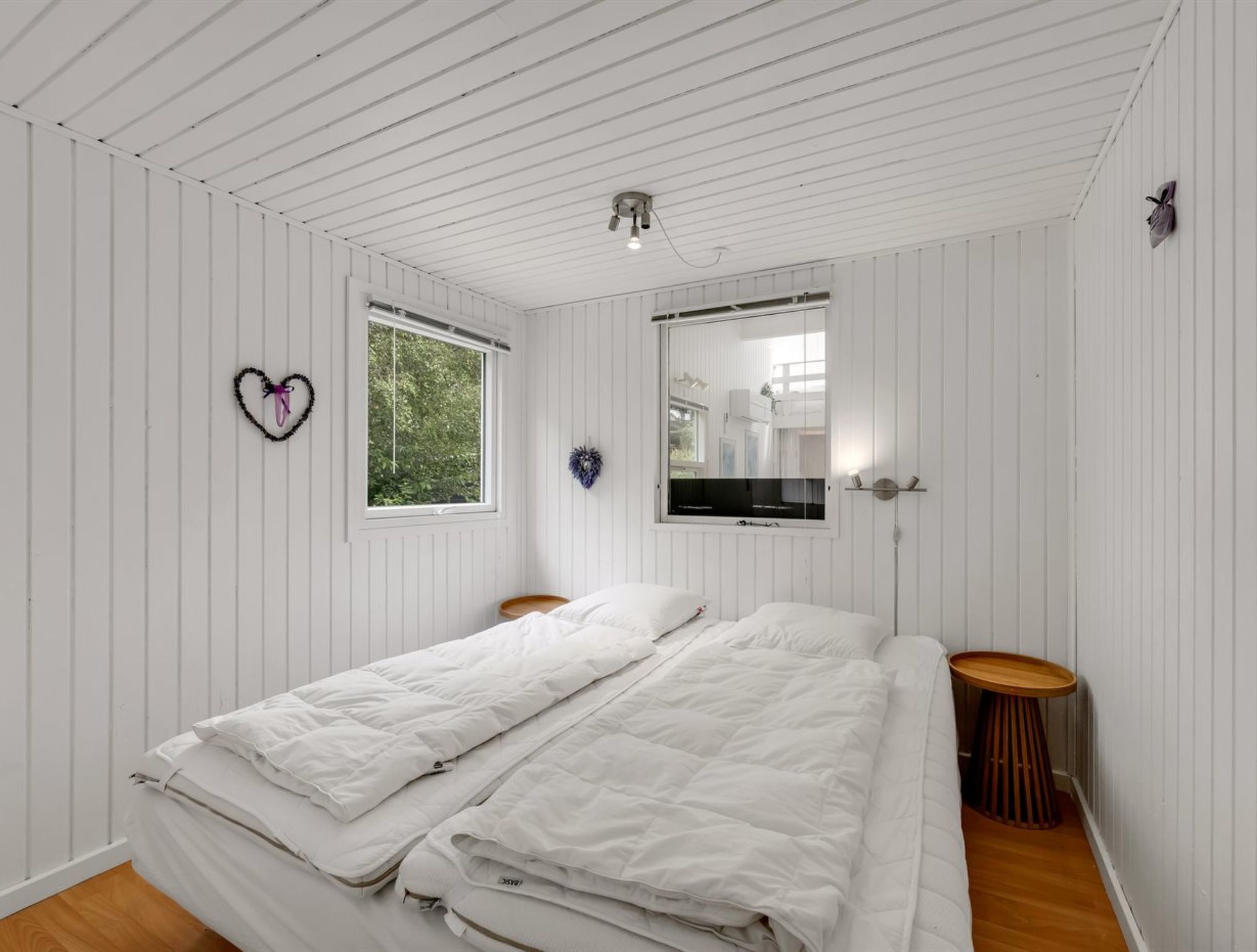 Un dormitorio con dos camas, una ventana, un espejo y una decoración con forma de corazón en la pared.
