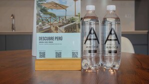Eine Broschüre mit dem Titel 'DESCUBRE PERÚ', QR-Codes und zwei Flaschen 'andea'-Wasser auf einem Holztisch.