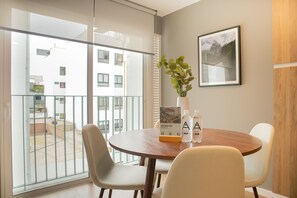 A modern dining area with a round wooden table, two chairs, a potted plant, and a framed picture on the wall.