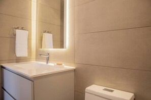A modern bathroom with a white sink, mirror, and toilet.