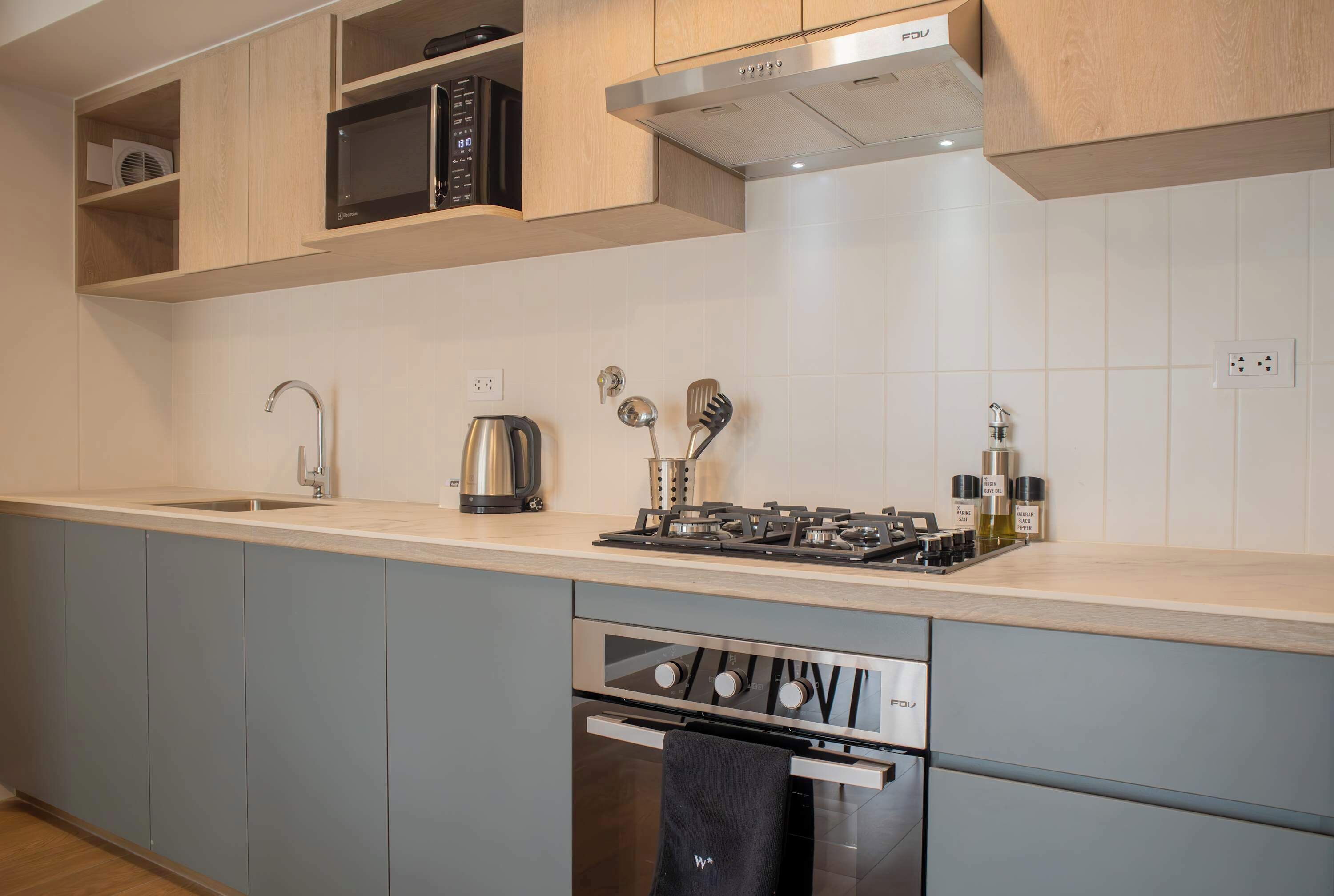 Une cuisine moderne avec des meubles gris, une hotte en acier inoxydable, un four à micro-ondes encastré, une bouilloire et une cuisinière à gaz.
