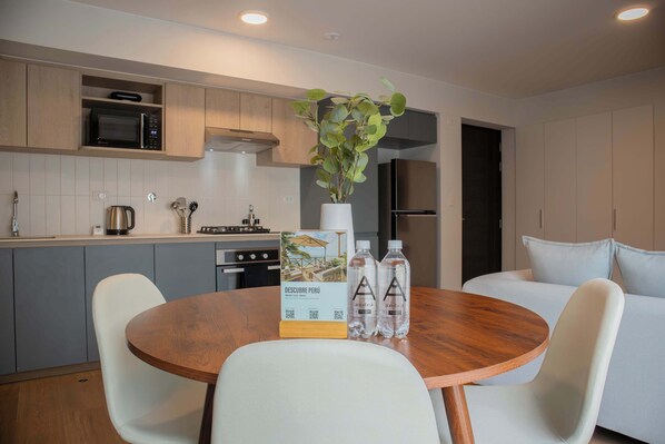 A modern kitchen with a microwave, stove, and sink. There is a dining table with chairs and a potted plant.