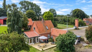 Une maison avec un toit recouvert de tuiles rouges, une terrasse avec des meubles d’extérieur et un jardin clos.