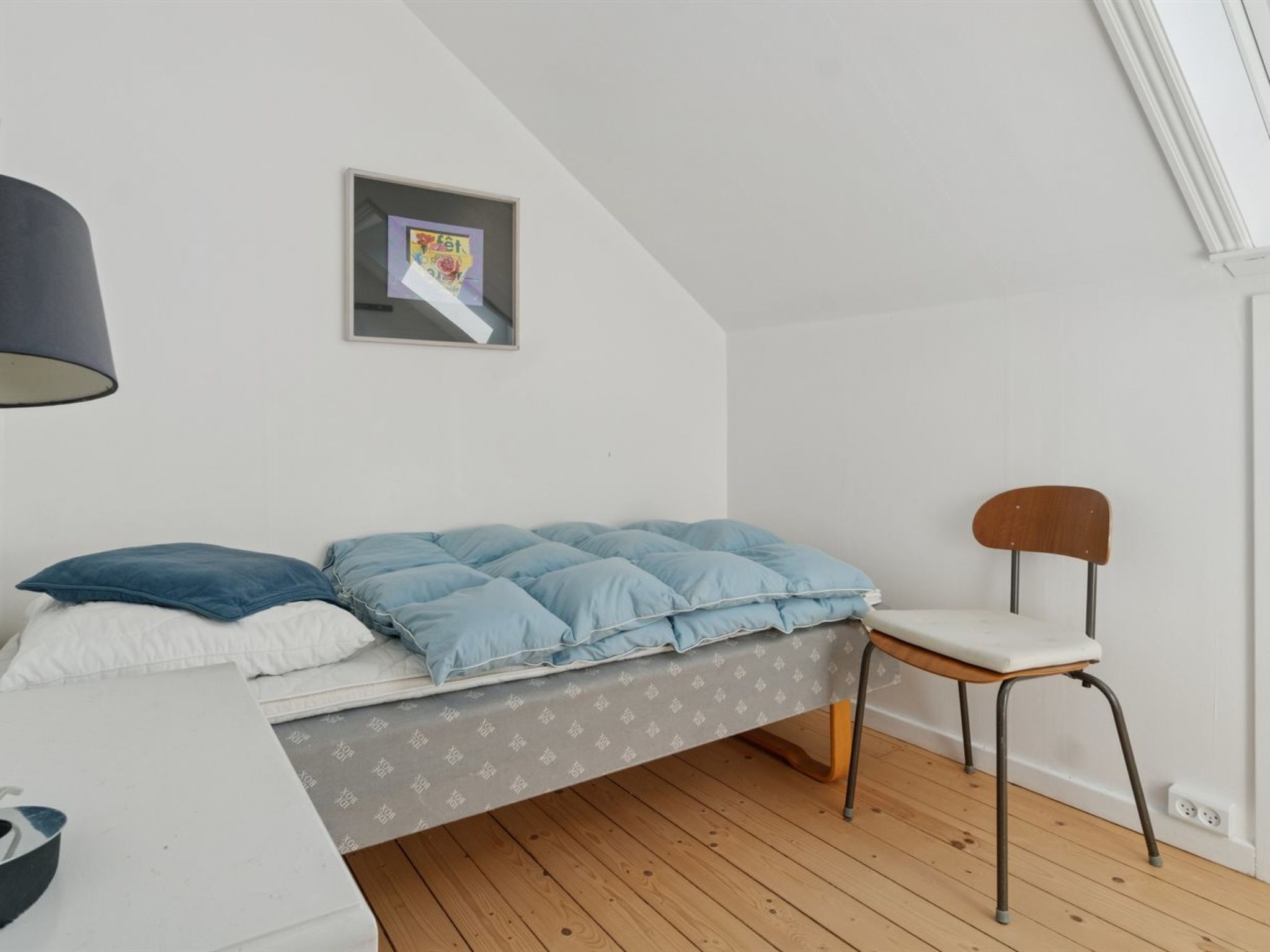 Une petite chambre à coucher, bien rangée, avec un lit, une chaise et un bureau.