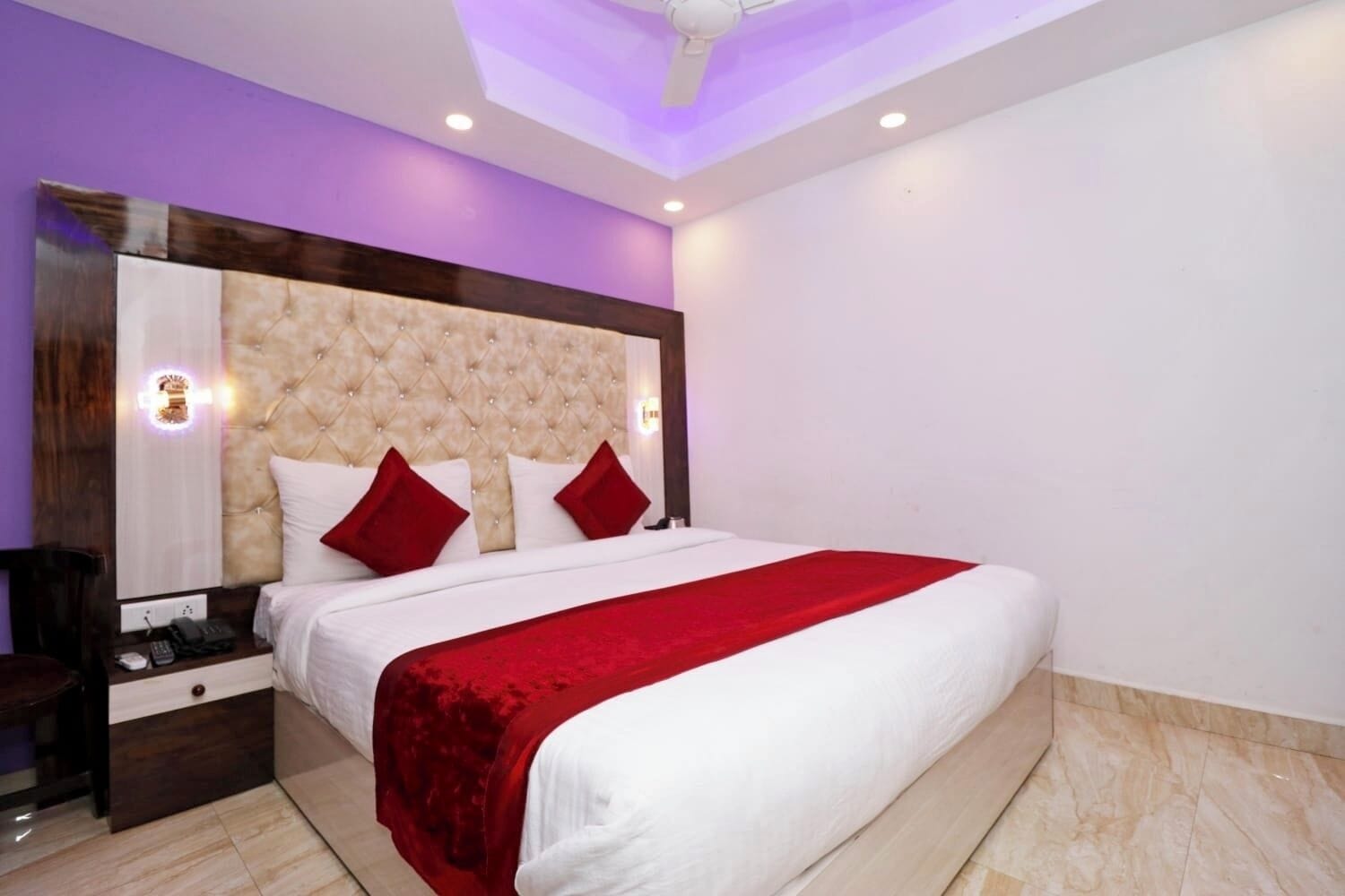 A modern hotel room with a large bed, a headboard with a tufted design, and a red throw blanket.