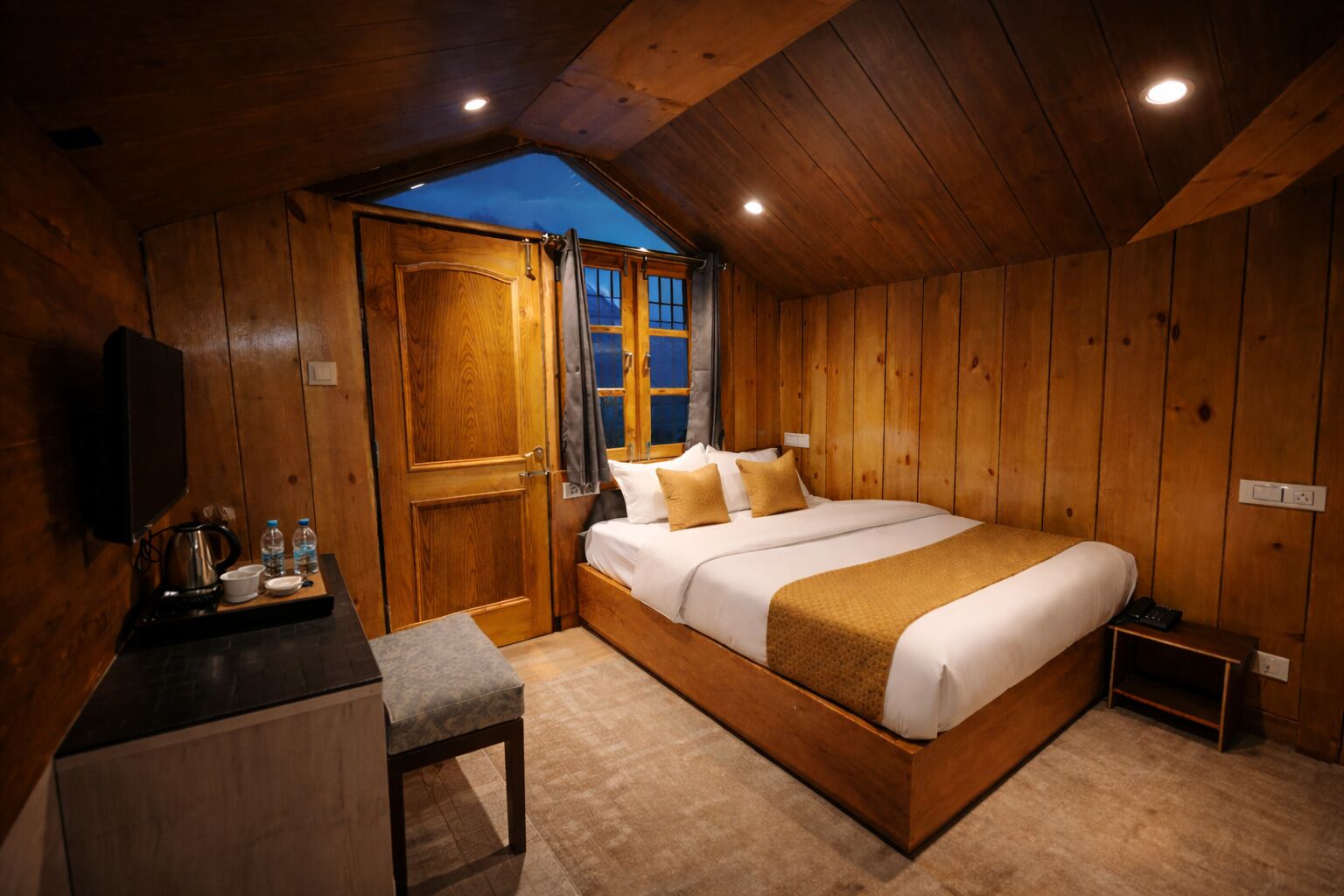 Une pièce en bois comprenant un lit, un bureau, une chaise, une fenêtre et un téléviseur.