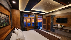 A hotel room with a large bed, wooden walls, a TV, and a view of the sunset through the windows. - Hotel Ranveer Palace (Narkanda)