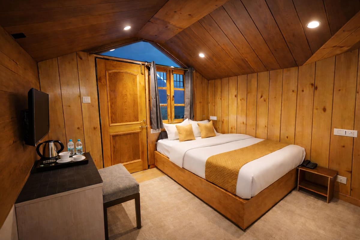A wooden room with a bed, a TV, a small table with a kettle, and a window.