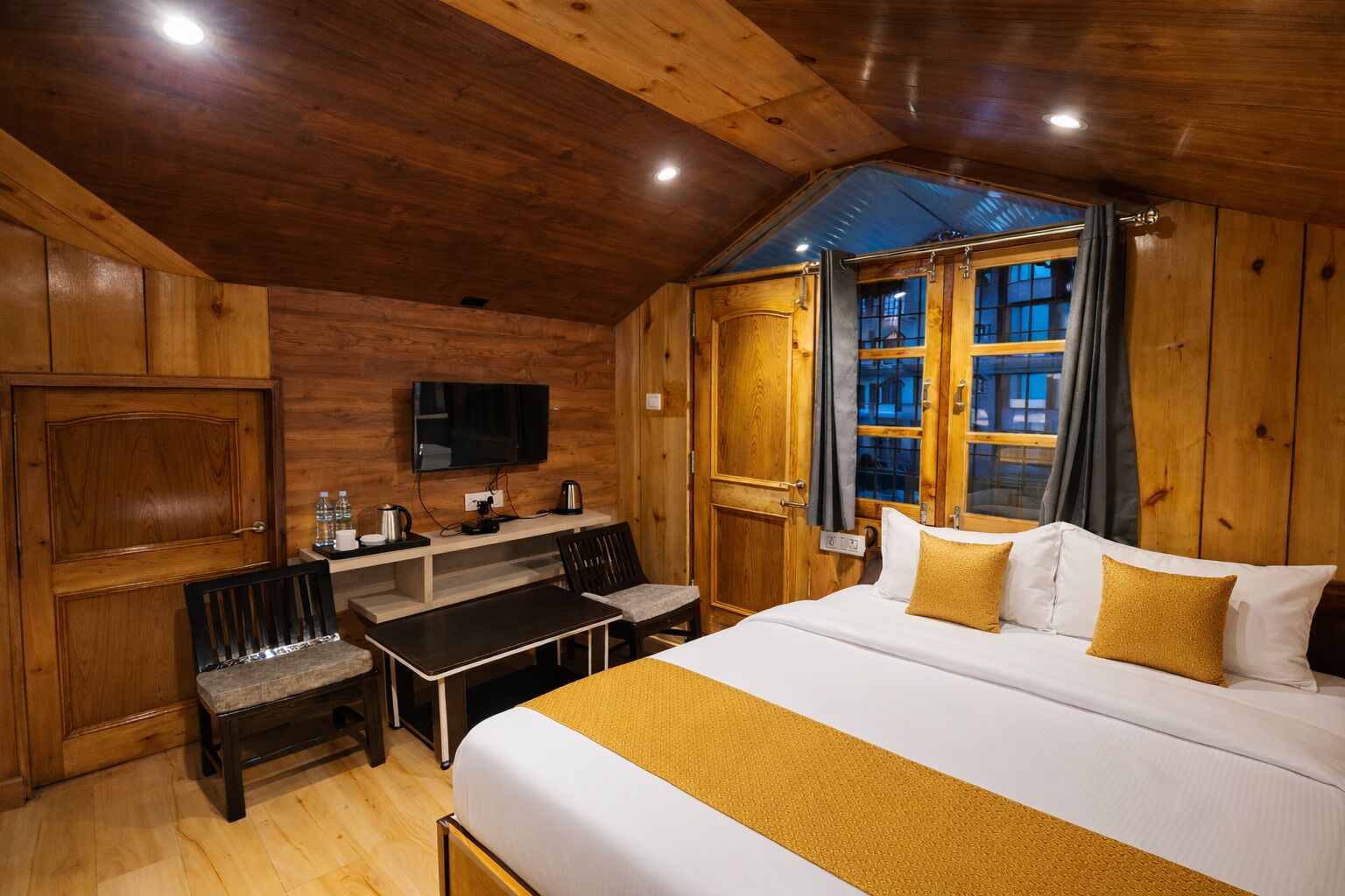 Una habitación de cabaña de madera con una cama, un escritorio, sillas y un televisor.