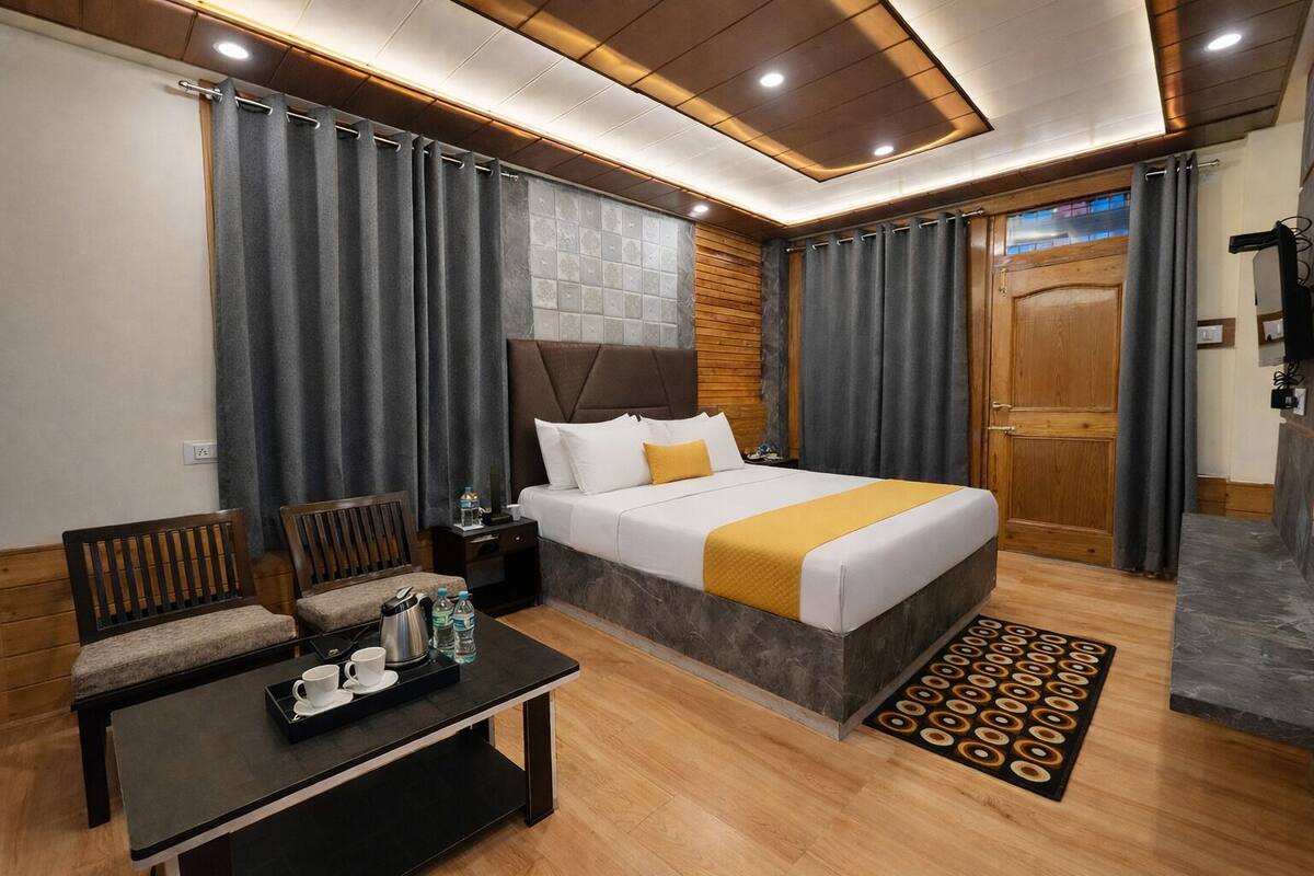 A hotel room with a bed, two chairs, a small table with a tray, a nightstand, and a wooden door.