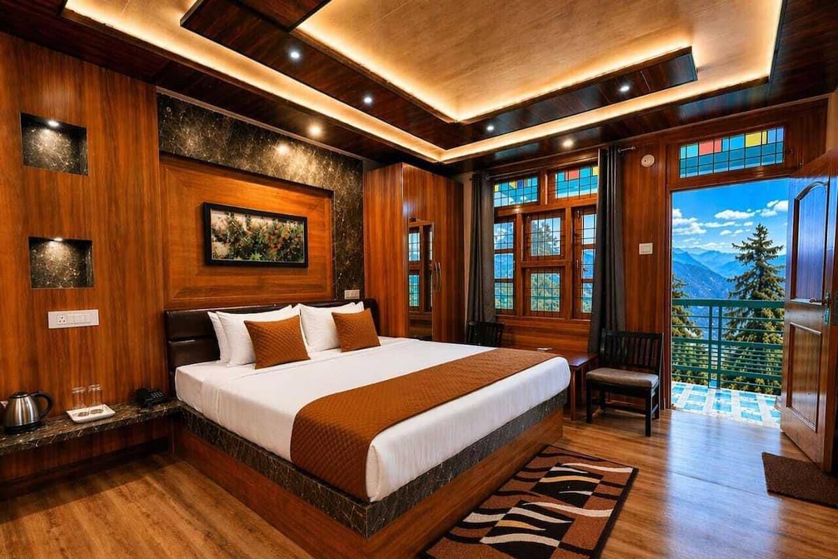A large bed with a wooden headboard, a nightstand, a chair, and a view of mountains through large windows.
