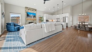 A spacious living area with a white sofa, blue armchair, and a dining table with chairs.