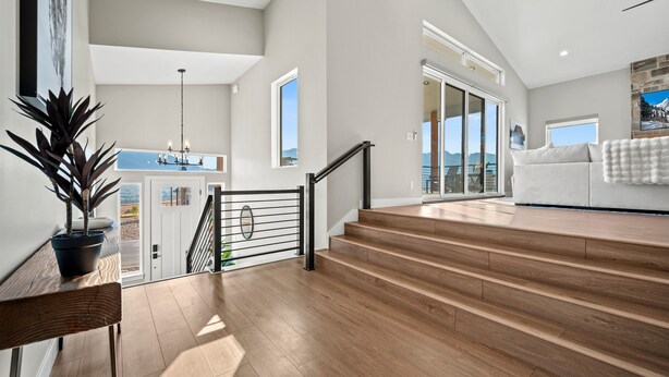 A spacious living area with a wooden staircase, a large potted plant, and a view of the outdoors.