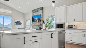 A modern kitchen with white cabinets, a large island, a stone accent wall, and a view of mountains.
